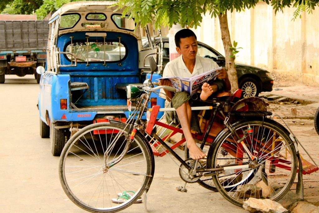 Nous sommes à Mandalay en Birmanie. Ce monsieur attend le client en lisant la presse propagande