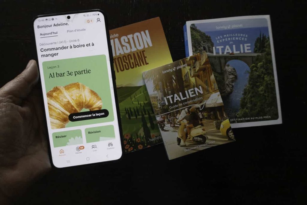 3 livres sur l'Italie et un écran de téléphone avec une application pour prendre des cours d'italien en ligne