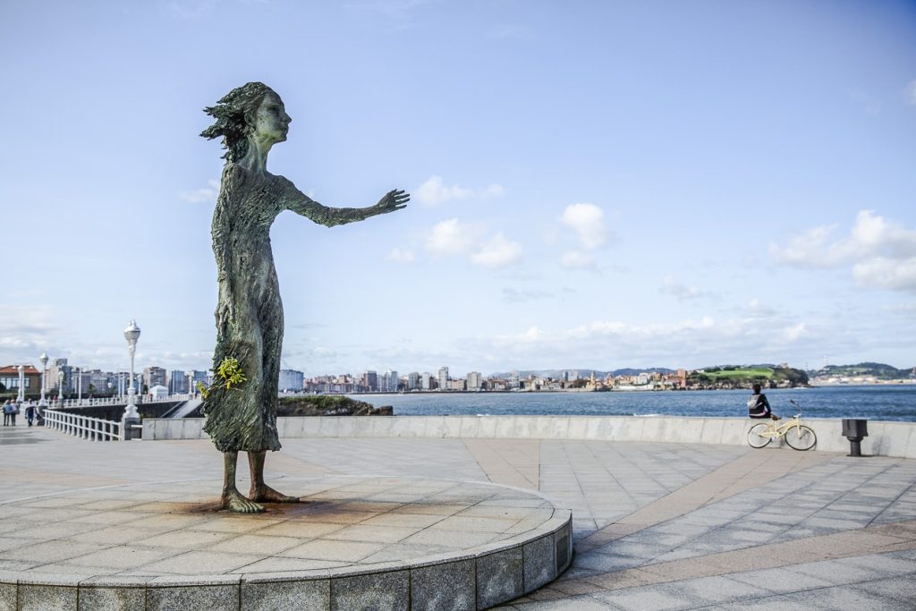 Sculpture en bronze d'une femme regardant la mer le bras tendu