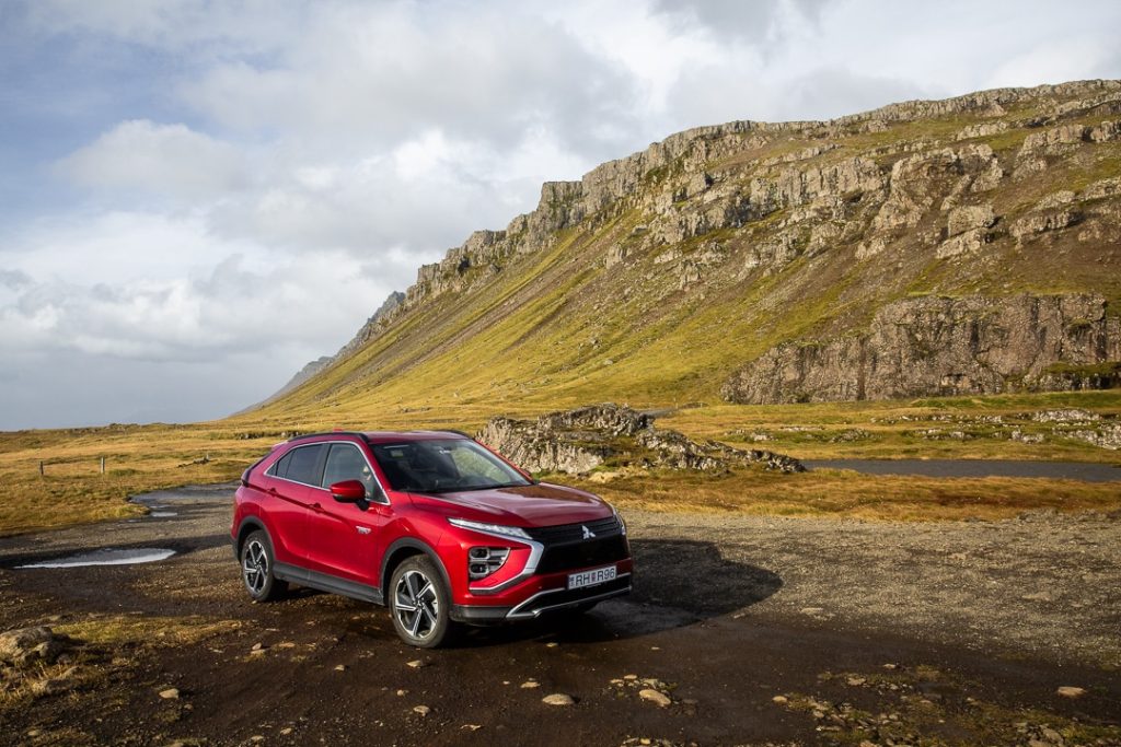 Un 4x4 suv rouge garé sur du sable noir dans les fjords du nord, avec en arrière plan une montagne verdoyante