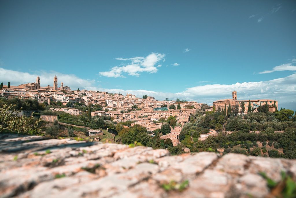 Vue panoramique du village médiéval de Montalcino en Toscane, avec ses maisons en pierre ocre, ses clochers et ses collines verdoyantes sous un ciel bleu parsemé de nuages